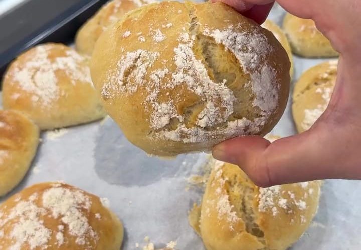 A basket of fresh, crusty no-knead spoon bread rolls with a flour-dusted top.