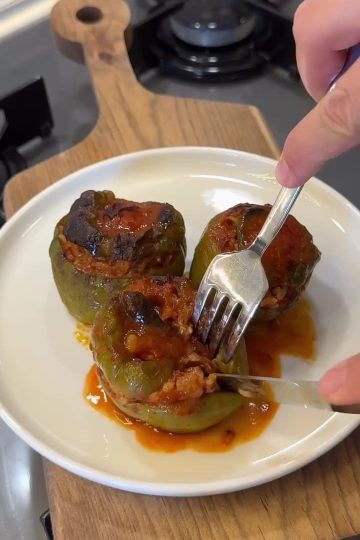 A dish of golden-brown Turkish stuffed peppers served with a side of sauce.