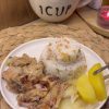 A tray of golden-brown pan-seared chicken butterfly pieces served with roasted potatoes and onions.