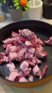 Placing raw cubed lamb meat into a heat-resistant baking tray.