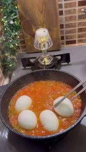 Placing boiled egg halves yolk-side down into the tomato sauce.