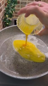 Placing a halved hamburger bun on top of raw eggs in a pan.