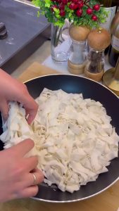 Spreading the first layer of shredded yufka pieces evenly in the frying pan.