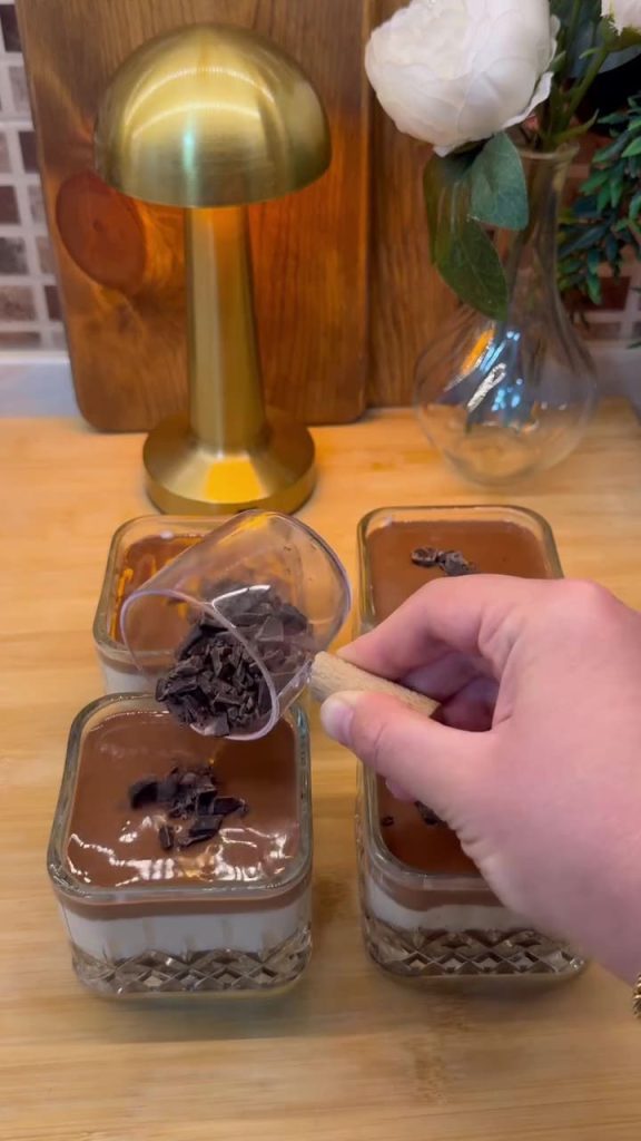 Pouring the final layer of lukewarm chocolate ganache over the pudding cups.