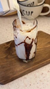 Pouring fresh milk into the iced glass while leaving space for the whipped foam.