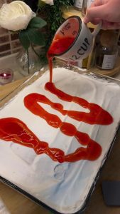 Pouring the final layer of red forest fruit sauce over the whipped cream layer.