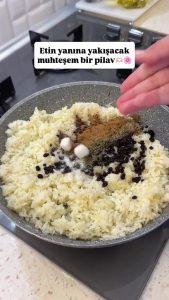 Pouring hot water over the spiced rice, sugar cubes, and currants in the pan.