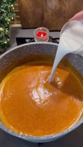 Adding a cup of milk to the blended roasted red pepper soup.