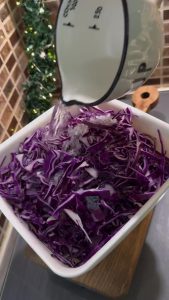 Pouring apple cider vinegar over sliced purple cabbage in a bowl.