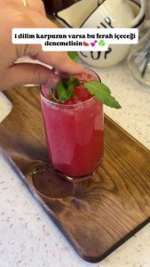 Pouring the bright pink sparkling watermelon juice over ice cubes in a glass.
