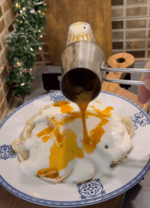 A plate of Turkish mantı dumplings topped with white garlic yogurt and red spicy butter sauce.