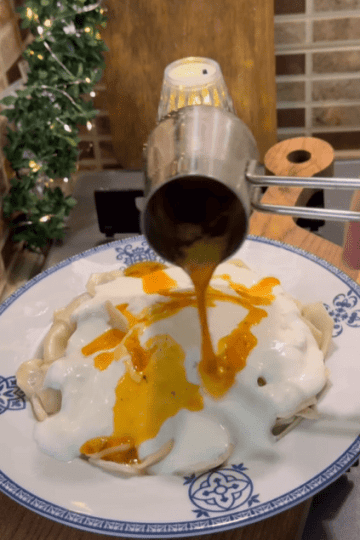 A plate of Turkish mantı dumplings topped with white garlic yogurt and red spicy butter sauce.