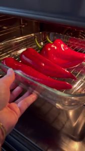 Roasting whole red capia peppers on a baking sheet until charred.