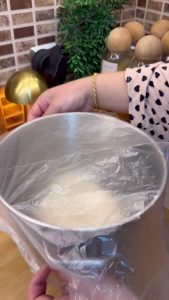 Rolling out pizza dough with a wooden rolling pin to fit a large oven tray.