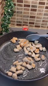 Cooking diced chicken breast in a frying pan until golden brown.
