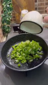 Sautéing chopped green peppers in a frying pan with vegetable oil.