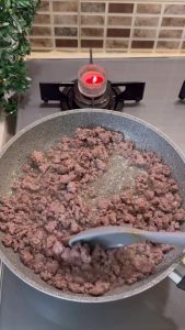 Sautéing ground beef with chopped onions, green peppers, and red capia peppers.