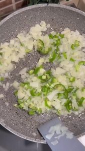 Sautéing onions and green peppers in a pan for the meat topping.