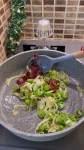 Sautéing onions and green peppers in a pan with vegetable oil.
