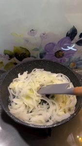 Sautéing sliced onions in a frying pan with vegetable oil over medium heat.