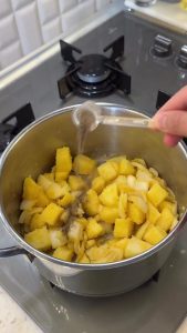 Stirring potatoes and onions with the cornmeal and butter mixture in a large pot.