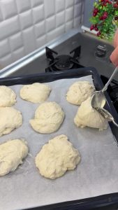 Using two oiled spoons to scoop mandarin-sized pieces of dough onto a baking tray.