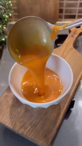 A finished bowl of creamy roasted red pepper soup with a swirl of milk.