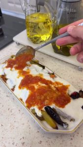 Pouring creamy garlic yogurt over the warm oven-roasted summer vegetables.