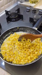 Simmering sweet corn in milk while stirring continuously on low heat for a creamy texture.