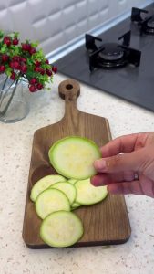 Slicing fresh green zucchinis into thin and even rounds on a wooden cutting board.