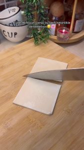 Slicing a square puff pastry sheet in half with a knife.