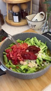 Simmering green beans with tomato paste and water in a covered pot on low heat.
