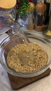 Soaking whole grain wheat in a glass bowl with hot water to soften.