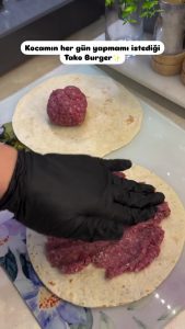 Spreading a thin, even layer of raw ground beef onto a flour tortilla sheet.