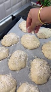 Sprinkling a generous amount of white flour over the raw dough portions on a tray.