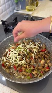 Covering the sautéed mushroom and pepper mixture with a thick layer of shredded cheese.