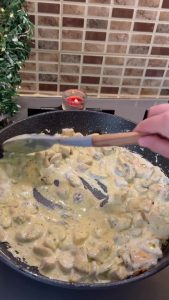 Mixing dried basil and curry into the simmering cream sauce.
