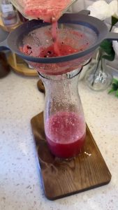 Straining the watermelon mixture through a sieve for a smooth, pulp-free texture.
