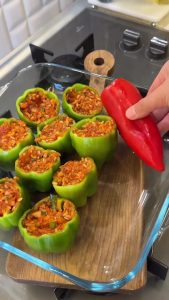 Filling the green bell peppers with the prepared raw rice and ground meat mixture using a spoon.