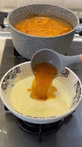 Adding a ladle of hot soup broth to the yogurt mixture to temper and prevent curdling.