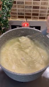 Stirring the milk pudding on the stovetop until it reaches a thick consistency.