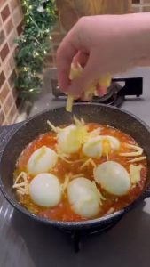 Sprinkling a layer of grated kashar cheese over the eggs and tomatoes.
