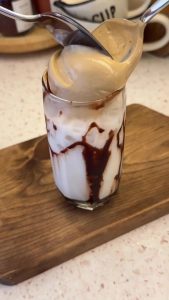 Spooning the thick, aerated honey coffee foam on top of the cold milk.