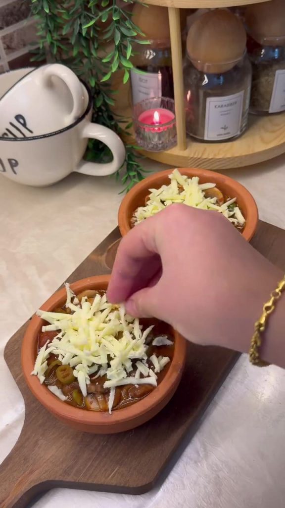 Adding a thick layer of grated kashar cheese over the mushroom pots.