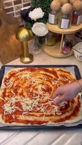 Adding sliced sucuk, corn, and colorful peppers to the homemade sheet pizza.