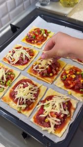 Distributing the mixed pizza toppings evenly over the sauce-covered puff pastry bases.