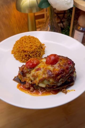 A golden-brown layered globe eggplant casserole with melted cheese and tomato slices