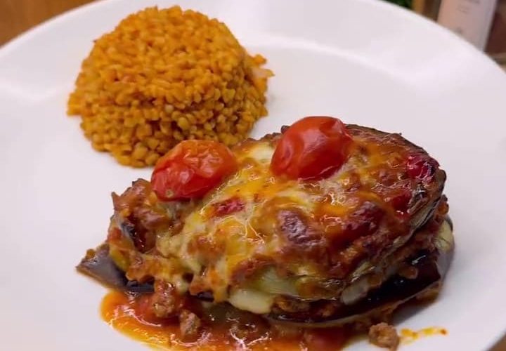 A golden-brown layered globe eggplant casserole with melted cheese and tomato slices