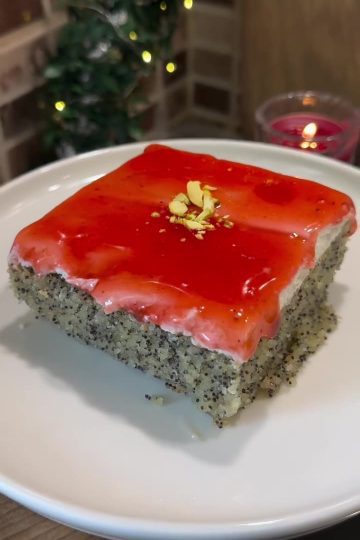 A slice of Turkish poppy seed revani cake with white cream and red forest fruit sauce layers.