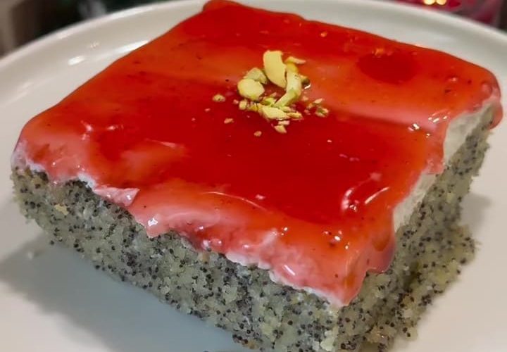A slice of Turkish poppy seed revani cake with white cream and red forest fruit sauce layers.